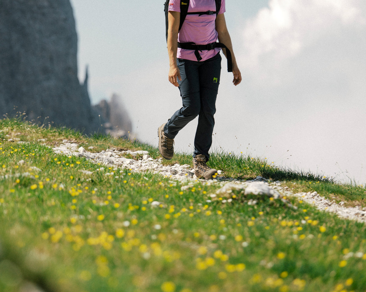 Une personne en randonnée sur un sentier herbeux bordé de fleurs, avec une montagne en arrière-plan